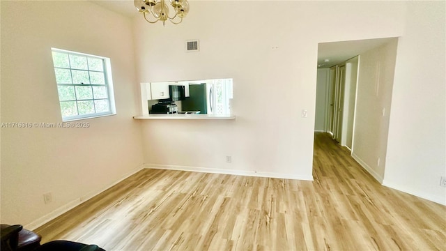 unfurnished room with a towering ceiling, light wood-type flooring, and a notable chandelier