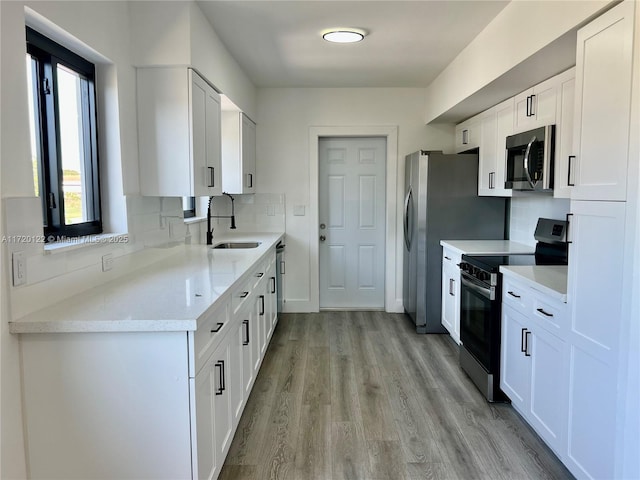 kitchen with backsplash, stainless steel appliances, white cabinetry, and sink