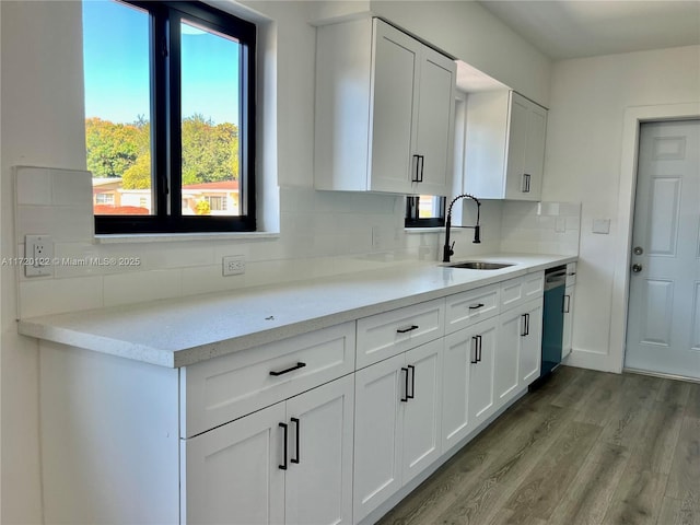 kitchen with backsplash, white cabinets, sink, light hardwood / wood-style flooring, and stainless steel dishwasher