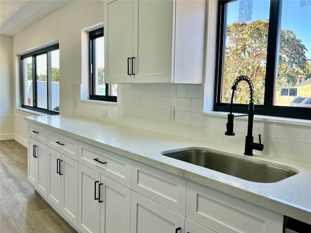 kitchen with light stone countertops, backsplash, white cabinets, and sink