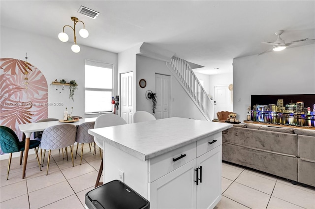 kitchen featuring ceiling fan, light tile patterned floors, decorative light fixtures, a center island, and white cabinetry