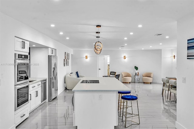 kitchen featuring a breakfast bar, decorative light fixtures, a kitchen island, white cabinetry, and stainless steel appliances