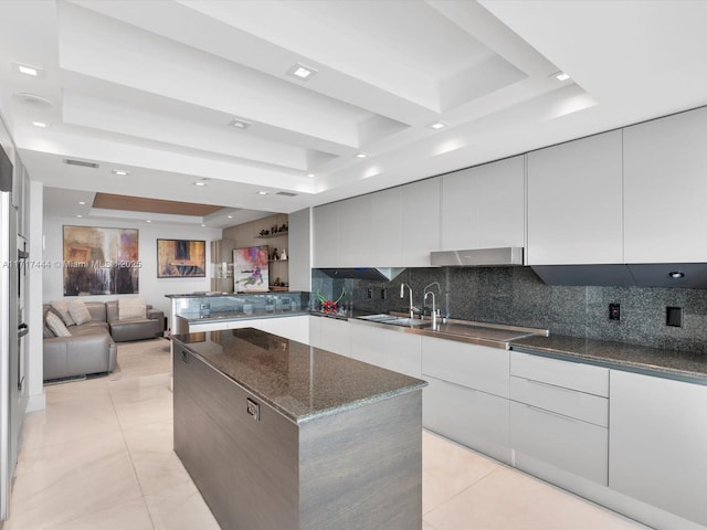 kitchen featuring light tile patterned floors, a raised ceiling, a spacious island, and dark stone countertops