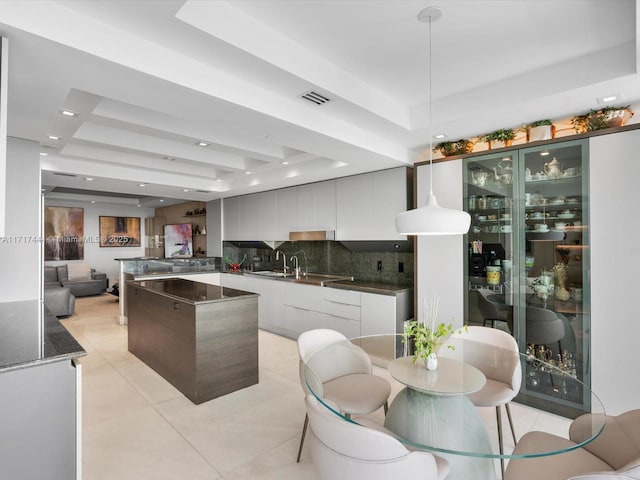 kitchen featuring white cabinetry, dark stone counters, pendant lighting, a tray ceiling, and decorative backsplash