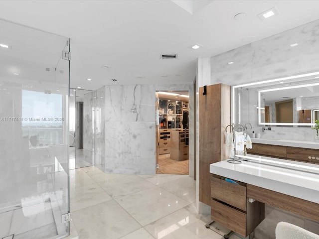 bathroom featuring visible vents, a shower stall, a walk in closet, vanity, and tile walls