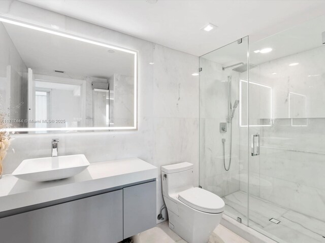 bathroom with a shower with door, vanity, tile walls, and toilet