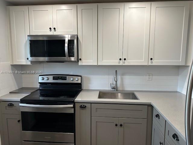 kitchen featuring tasteful backsplash, white cabinets, appliances with stainless steel finishes, and sink