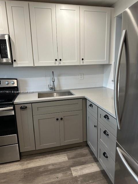 kitchen with hardwood / wood-style floors, appliances with stainless steel finishes, white cabinetry, sink, and gray cabinets