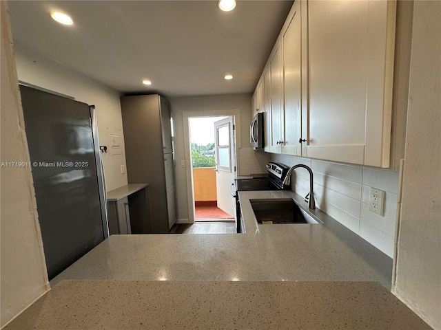 kitchen featuring decorative backsplash, sink, white cabinetry, stainless steel appliances, and light stone counters