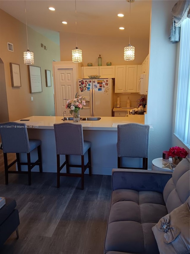 kitchen featuring a kitchen bar, dark hardwood / wood-style flooring, decorative light fixtures, and white appliances