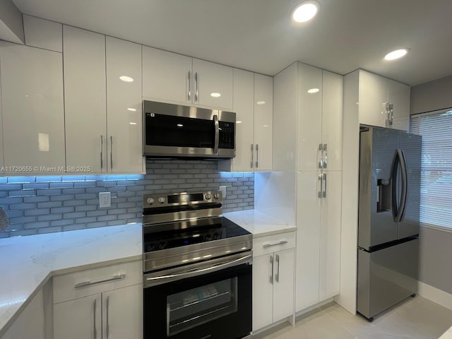 kitchen with backsplash, light tile patterned floors, light stone countertops, stainless steel appliances, and white cabinets