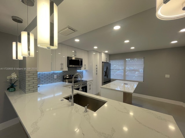 kitchen featuring kitchen peninsula, hanging light fixtures, light stone countertops, stainless steel appliances, and white cabinets