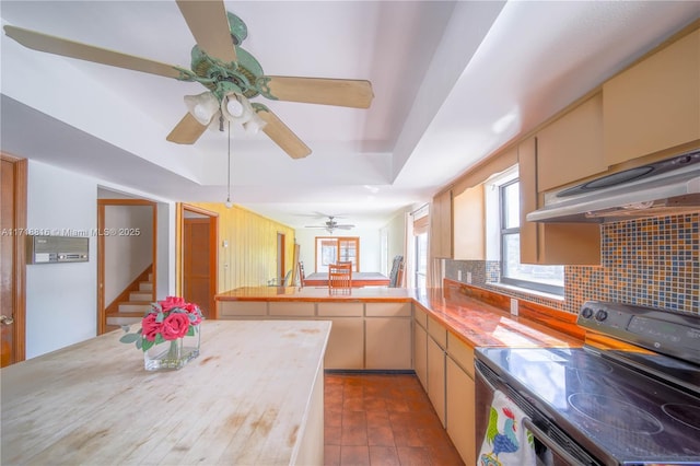 kitchen with kitchen peninsula, decorative backsplash, ventilation hood, a raised ceiling, and electric stove