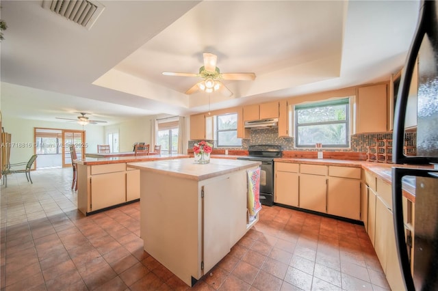 kitchen featuring ceiling fan, black range with electric cooktop, a raised ceiling, kitchen peninsula, and a kitchen island