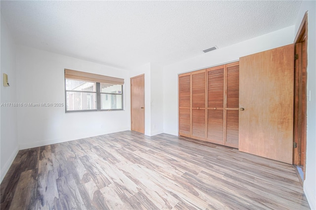 unfurnished bedroom with light hardwood / wood-style floors, a textured ceiling, and a closet
