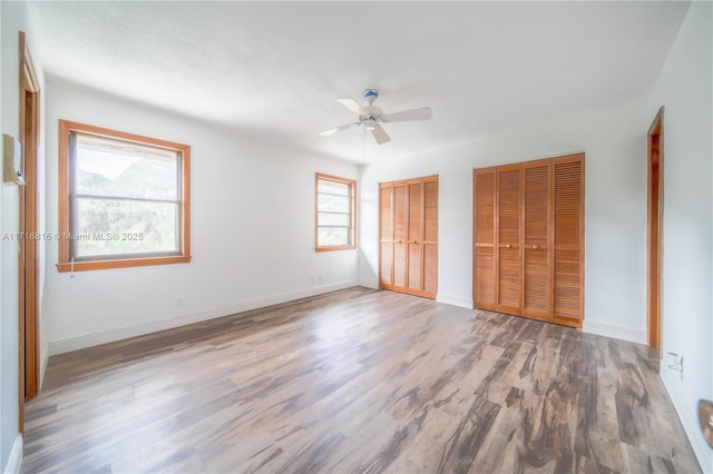 unfurnished bedroom with hardwood / wood-style floors, ceiling fan, multiple windows, and two closets