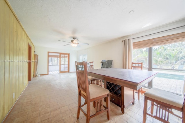 dining room with ceiling fan, wood walls, and a textured ceiling