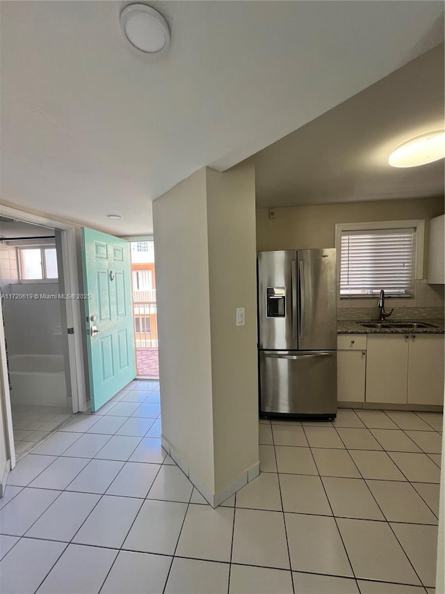 kitchen featuring sink, light tile patterned floors, stainless steel refrigerator with ice dispenser, dark stone counters, and white cabinets