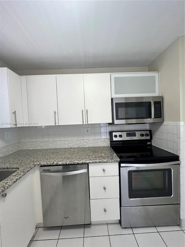 kitchen with white cabinets, light tile patterned flooring, light stone counters, and stainless steel appliances