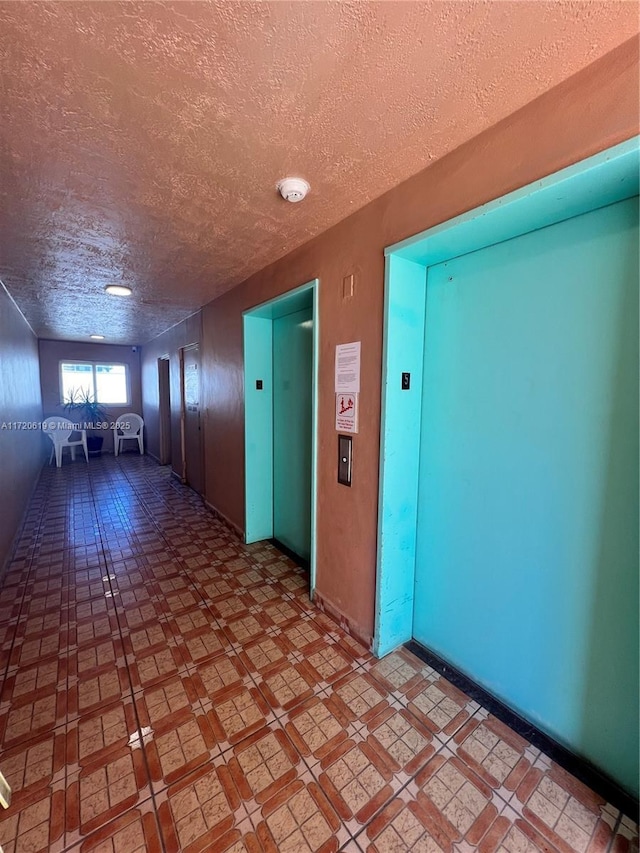 hallway with elevator and a textured ceiling