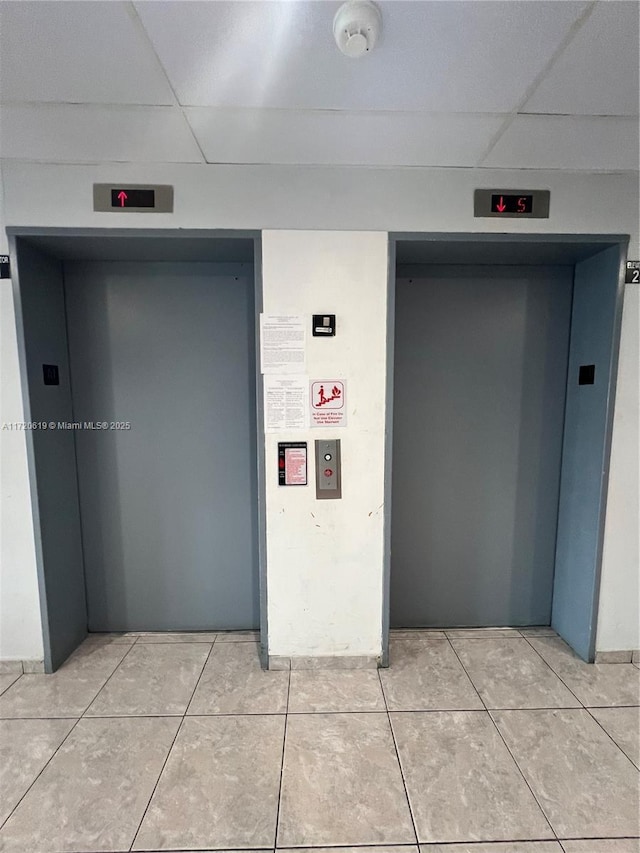 hall with a drop ceiling, elevator, and light tile patterned flooring