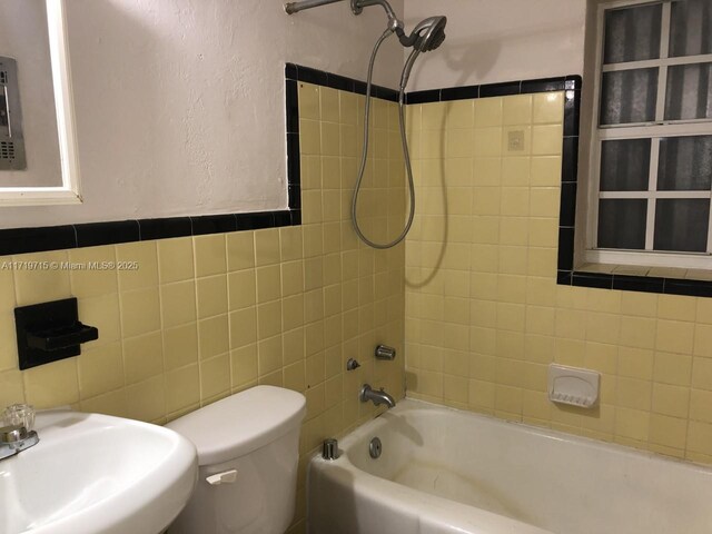 full bathroom with tile walls, toilet, tiled shower / bath, and sink