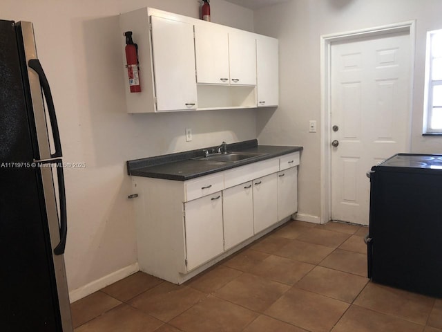 kitchen featuring sink, black fridge, tile patterned floors, stove, and white cabinets