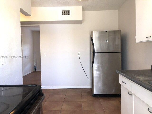 kitchen with stainless steel fridge, white cabinetry, and dark tile patterned floors