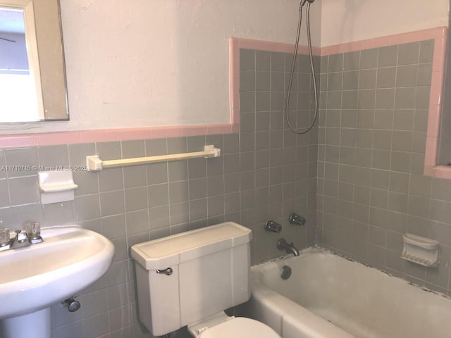 full bathroom featuring sink, toilet, tiled shower / bath, and tile walls