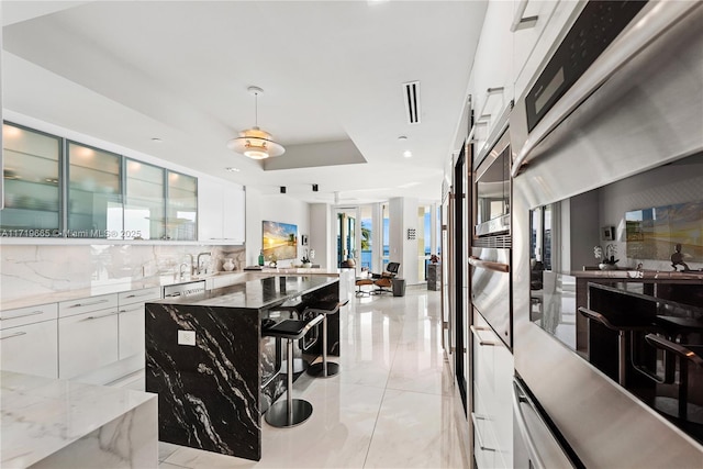 kitchen featuring a center island, dark stone counters, white cabinets, a raised ceiling, and tasteful backsplash