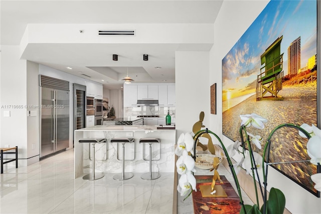 kitchen with a raised ceiling, kitchen peninsula, appliances with stainless steel finishes, white cabinetry, and a breakfast bar area