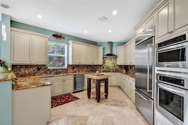 kitchen featuring cream cabinetry, stainless steel appliances, visible vents, decorative backsplash, and wall chimney range hood