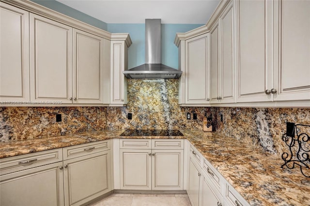 kitchen with tasteful backsplash, dark stone counters, wall chimney exhaust hood, black electric cooktop, and cream cabinetry