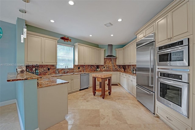 kitchen featuring wall chimney exhaust hood, dark stone counters, visible vents, cream cabinetry, and appliances with stainless steel finishes