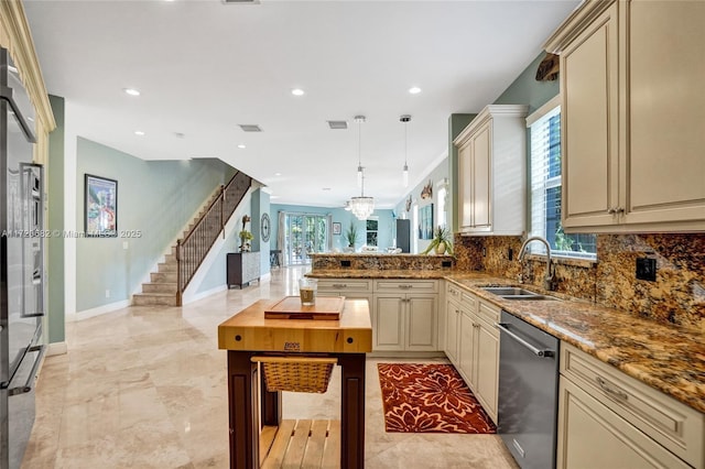 kitchen featuring dishwasher, backsplash, sink, hanging light fixtures, and cream cabinetry