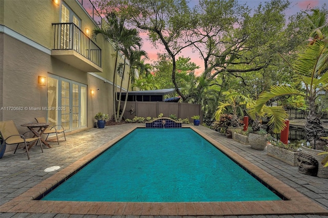 pool at dusk featuring french doors and a patio