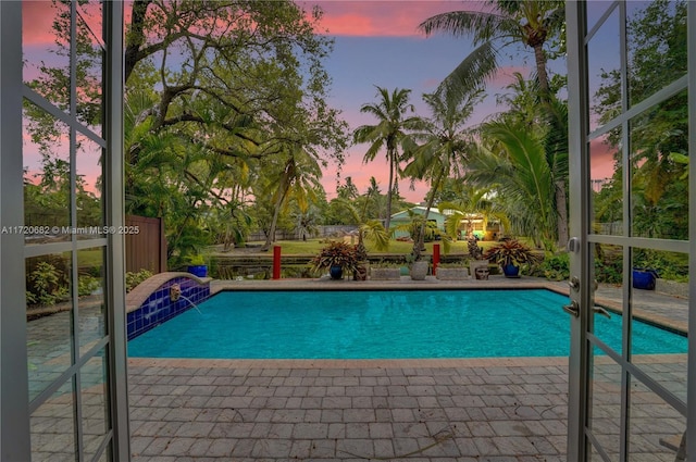 pool at dusk featuring pool water feature and a patio area