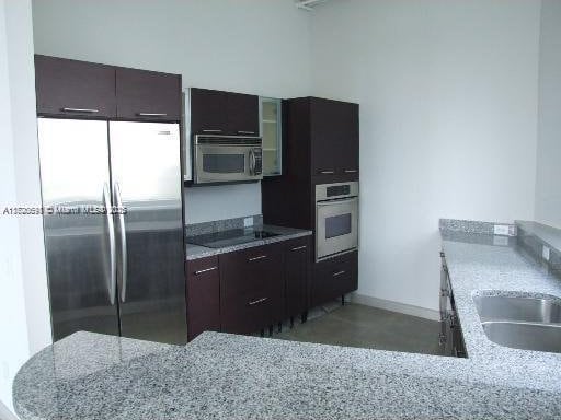 kitchen featuring dark brown cabinetry, light stone counters, sink, and appliances with stainless steel finishes