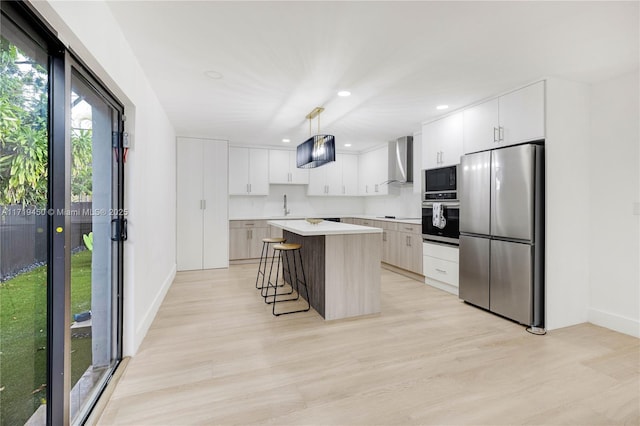 kitchen with black appliances, white cabinets, wall chimney range hood, decorative light fixtures, and a kitchen island