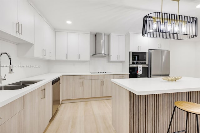 kitchen with pendant lighting, wall chimney range hood, sink, light wood-type flooring, and stainless steel appliances