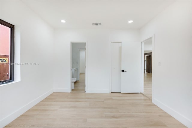 unfurnished bedroom with connected bathroom, light hardwood / wood-style floors, and multiple windows