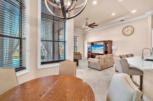 dining room featuring ceiling fan with notable chandelier, a tray ceiling, crown molding, and sink