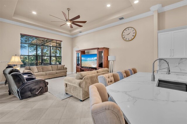 living room featuring ceiling fan, crown molding, sink, and a tray ceiling