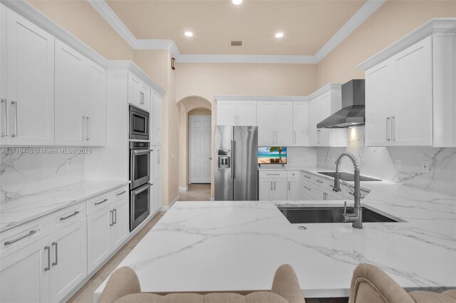 kitchen featuring appliances with stainless steel finishes, a kitchen breakfast bar, tasteful backsplash, wall chimney range hood, and white cabinetry