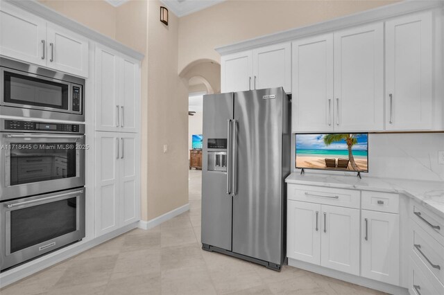 kitchen with decorative backsplash, white cabinetry, light stone countertops, and appliances with stainless steel finishes