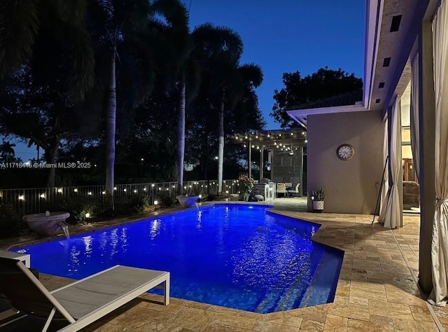 pool at night with pool water feature and a patio