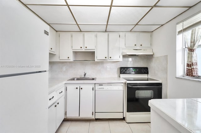 kitchen with a paneled ceiling, white appliances, sink, light tile patterned floors, and white cabinets