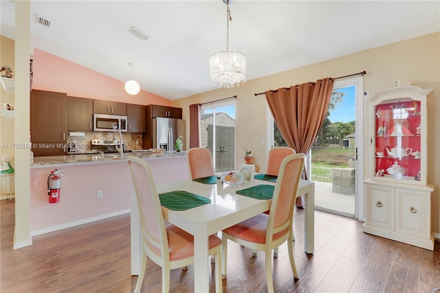 dining area with a chandelier, wood-type flooring, a wealth of natural light, and lofted ceiling