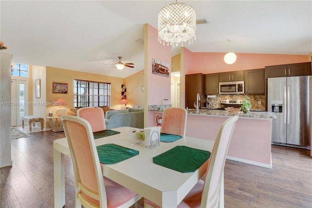 dining area featuring ceiling fan with notable chandelier, dark hardwood / wood-style floors, vaulted ceiling, and sink