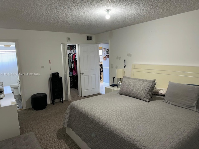 carpeted bedroom featuring a spacious closet, a closet, a textured ceiling, and ensuite bathroom